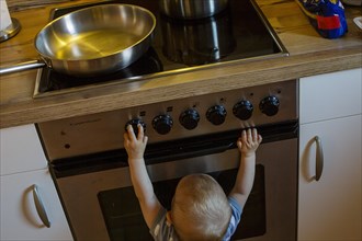 Symbol photo on the topic of dangers for small children in the household. A small child plays with the knobs of a cooker. Berlin
