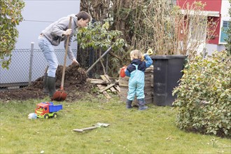 Toddler and father digging at a pile of earth in the garden.