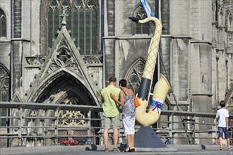 Tourists at decorated saxophone on bridge in front of the Collegiate Church of Notre-Dame at Dinant