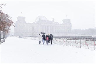 Five people stand in front of the Bundestag in the driving snow in Berlin