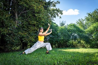 Serene adult woman doing qigong exercise in the park. Connection to nature and the vital energy of the universe