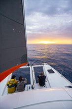 Three young men sitting on catamaran looking into the sunset