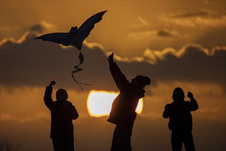 The silhouette of three people emerges while flying a kite in front of sunset in Berlin