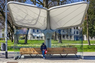 Rain and sun protection over park bench and man with knitted cap