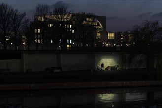 A homeless man silhouetted on the banks of the Spree in front of the Federal Chancellery in Berlin