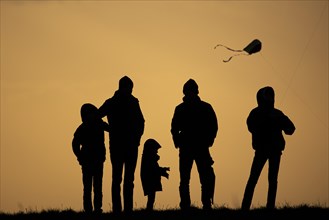 The silhouette of three children and two adults stands out while flying a kite in front of sunset in Berlin