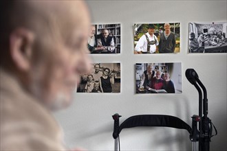 Subject: Old man sitting in front of a wall with pictures