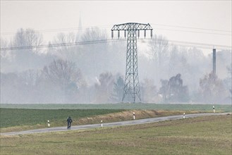 A cyclist rides on a country road in front of an electricity pylon