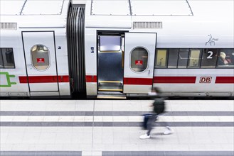 A person with a suitcase stands in front of a stationary Deutsche Bahn ICE train in Berlin main station