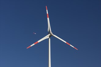 Jet airliner seen through blades of wind turbine against blue sky