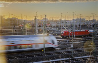 A Deutsche Bahn Intercity train passes through Halle an der Saale while an electric locomotive from DB Cargo waits in the background with a goods train to continue its journey. Halle