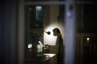 Symbolic photo on the subject of masks at the workplace. A woman sits in her desk in the office in the evening wearing an FFP2 mask. Berlin