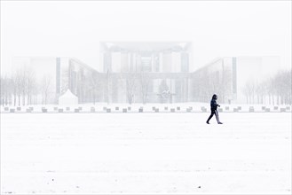 A person is silhouetted in front of the Chancellery in the driving snow in Berlin