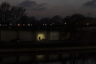 A homeless man silhouetted on the banks of the Spree in Berlin