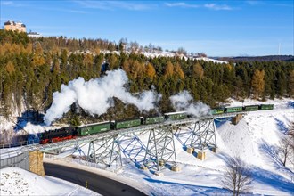 Steam train of the Fichtelbergbahn railway Steam locomotive on a bridge in winter Aerial view in Oberwiesenthal
