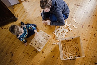 Symbolic photo on the subject of creative play among children. A boy builds with wooden building blocks with an adult. Berlin