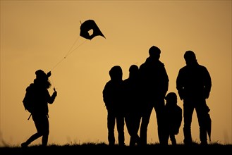 The silhouette of three children and three adults stands out while flying a kite in front of sunset in Berlin
