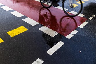 A cyclist on the cycle path is reflected in the wet street in Berlin