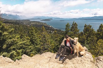 Young woman and her dog hiking to the top of a mountain. View of a large lake