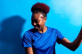 Young african american woman isolated on a blue background smiling and dancing