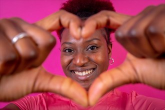 Young african american woman isolated on a pink background smiling and heart gesture
