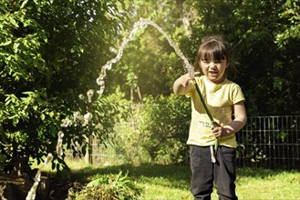 Happy little girl playing with a garden hose. Preschool child having fun with watering trees and plants in domestic garden