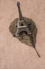 Little model Eiffel Tower and a dry leaf on brown background