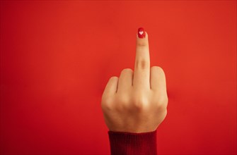 Fuck you hand sign. Female hand with bright red manicure showing middle fingers gesturing. Aggressive reaction. Close up. Red background