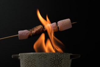Marshmallows strung on fire from a ceramic bowl on a wooden board isolated on black background and copy space