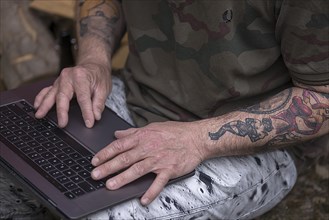 Tattooed arms of a man at his laptop in his home office