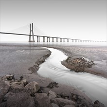 Long exposure of the famous bridge Ponte Vasco da Gama at low tide on the river Tejo with a small water tributary in Lisbon