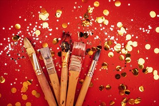 Set of colorful artist brushes. Bright red background with silver glitters and gold round confetti. Painted brushes. Copy space. Celebration and art concept