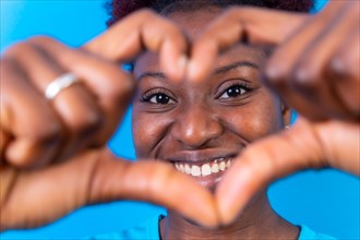 Young african american woman isolated on a blue background smiling and heart gesture
