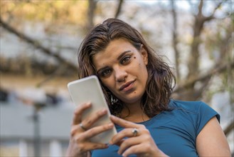 A beautiful latin woman using her smartphone outdoors looking at camera