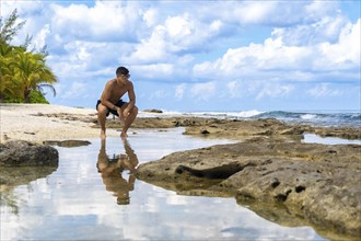 Pensive man squatting on beach. Beautiful tropical scenery. Concept Vacation