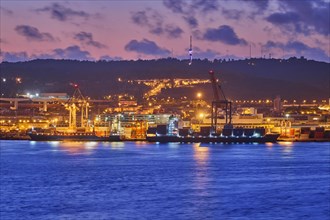 View of Lisbon port with sea container ships with port cranes in the evening twilight over Tagus river. Lisbon