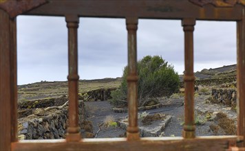 View through the glazing bars of a wooden gate onto an agricultural property on the volcano