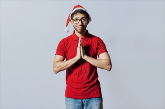 Man in christmas hat with hands together making a wish isolated. Guy with hands together making a christmas wish