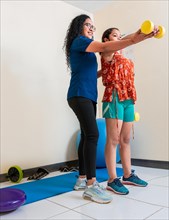 Rehabilitation physiotherapy with dumbbells. Physiotherapist helping patient with dumbbells on rehabilitation ball