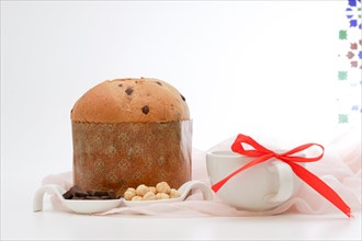 Panetone on a pink cloth ceramic spoons with hazelnuts and chocolate and white mug with a red ribbon
