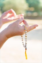 Close-up of a woman's hands holding a sunlit Buddhist mala praying in a field at sunset
