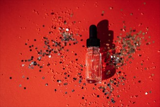 Transparent serum or oil glass bottle with pipette. Bright red background with silver glitters and confetti. Mock up. Concept of cosmetic and celebration. Copy space
