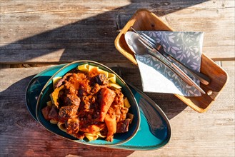 Plate of goulash with noodles and cutlery on a wooden table