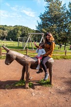A boy and a mother playing on the wooden horse in the leisure area at Laguna Grande in the Garajonay natural park on La Gomera