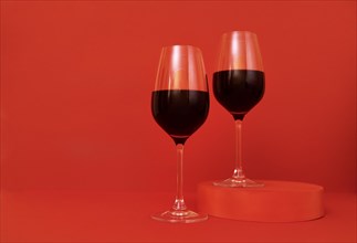 Two glasses of wine on the podium. Red bright background. Minimalism. Close up. Copy space. Valentines Day concept. Mockup for holidays design