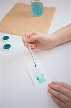 Woman's hands painting with a watercolor brush on a blank piece of paper at her workbench