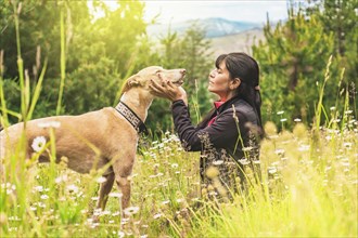 Latin woman and her dog together. Friendship between dog and pet owner. Woman sitting with her greyhound in nature