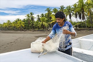 Concentrated fisherman preparing his net in his boat. Coastal landscape of palm trees in the central pacific