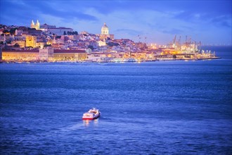 Night view of Lisbon over Tagus river from Almada with ferry and tourist boat in evening twilight. Lisbon