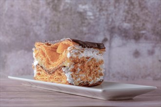 Close-up of a mille-feuille filled with cream and almonds covered with chocolate on a white plate